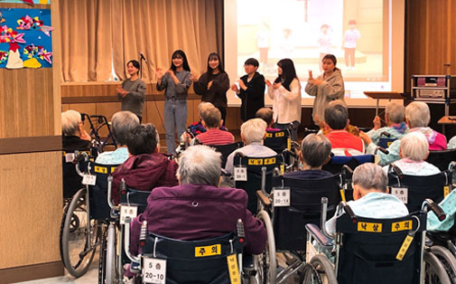 휠체어를 탄 어르신들 앞에서 장기자랑을 하고 있는 간호사랑 동아리 부원들 모습